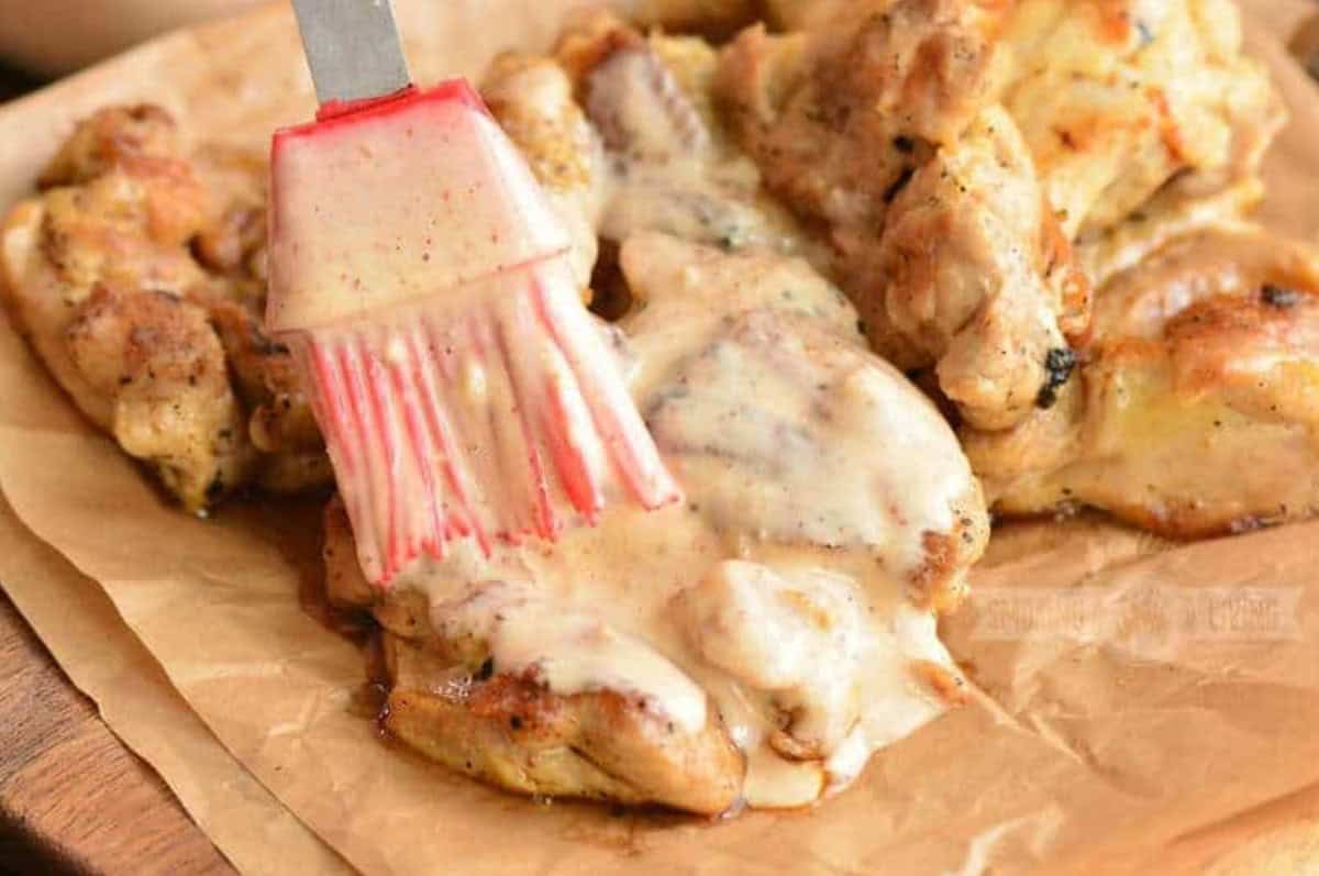 Brushing white BBQ sauce onto grilled chicken that is on wax paper.