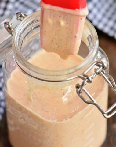 Dipping a brush into a jar of white BBQ sauce.