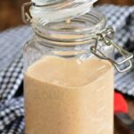 White BBQ sauce in a jar with the lid partially closed.
