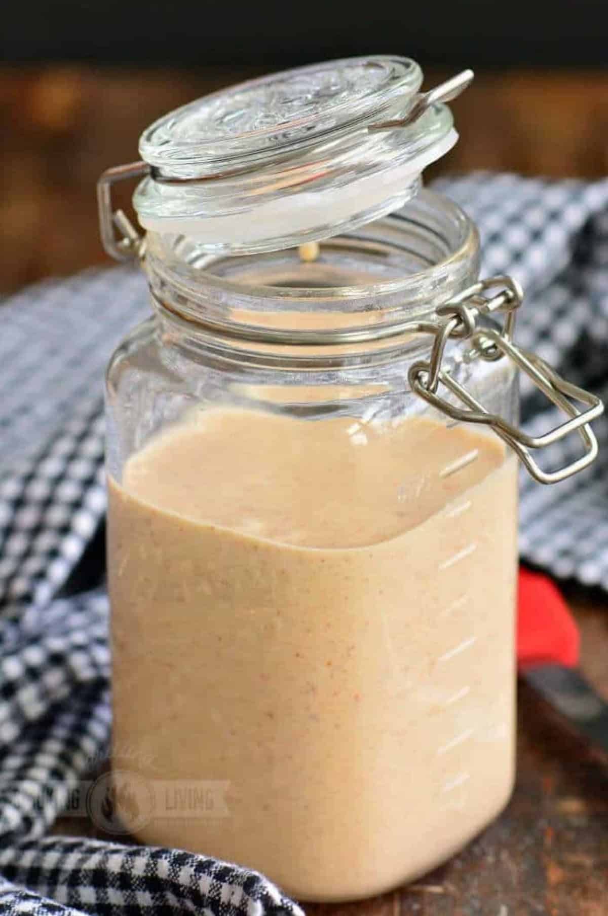 White BBQ sauce in a jar with the lid partially closed.