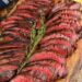 thinly sliced hanger steaks on a cutting board with a sprig of thyme on top